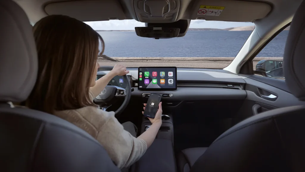 Person bruker infotainment og telefon i bil nær vann.