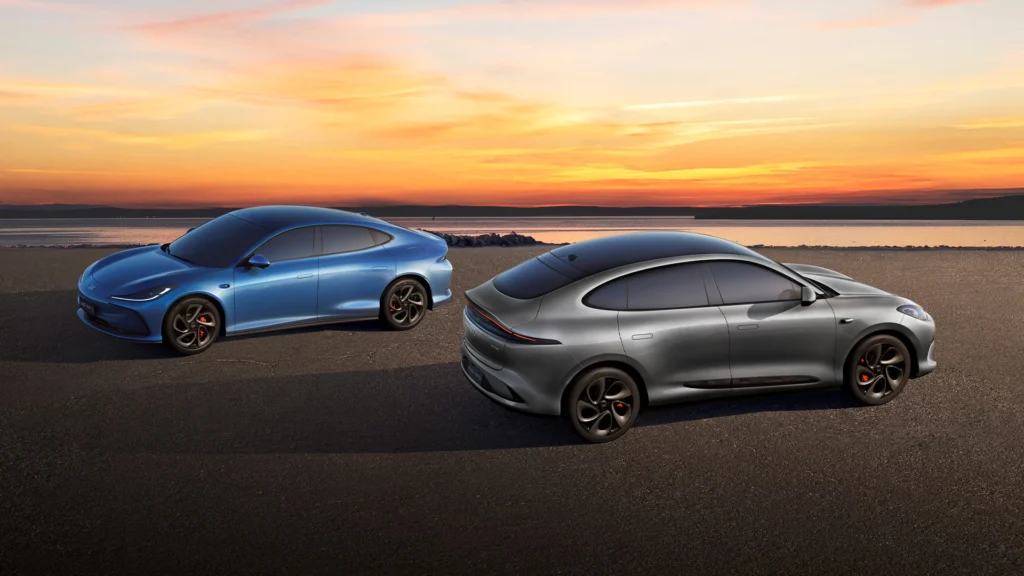 To elektriske biler parkert ved vannet i solnedgang.