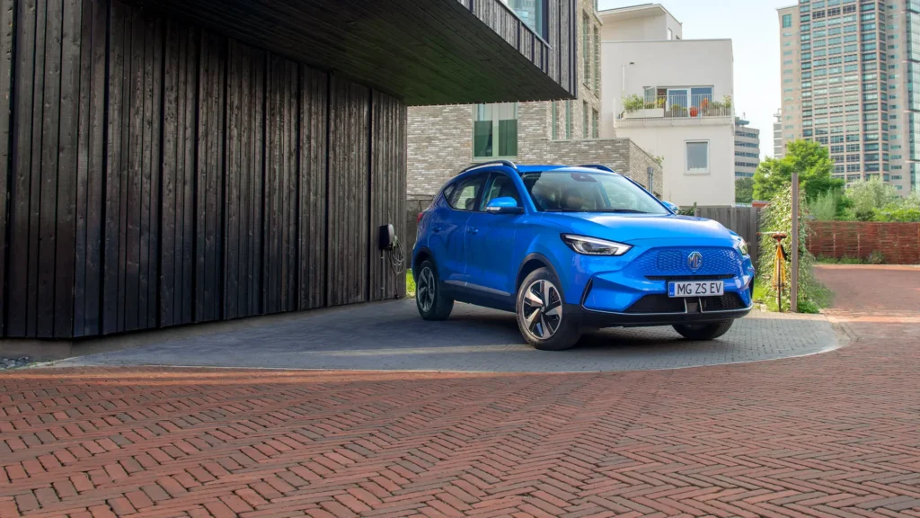 Blå MG elbil parkert ved moderne bygg med svart panel.
