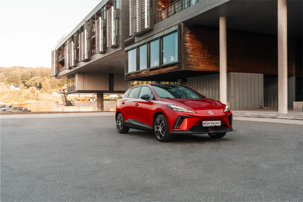 Rød elbil parkert foran moderne bygg med store vinduer.