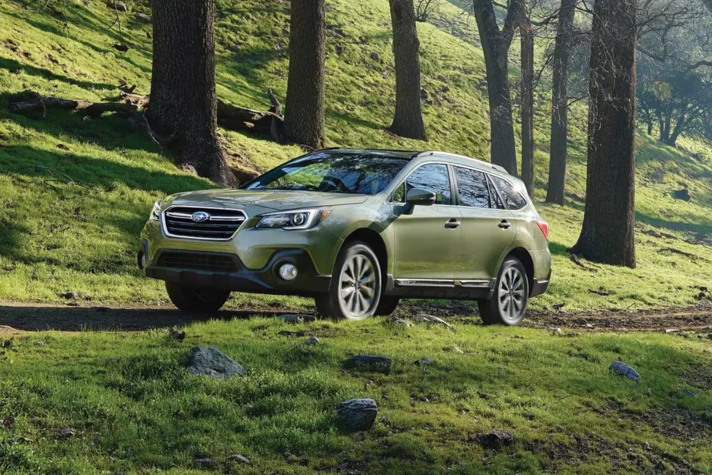 Grønn Subaru Outback parkert i sollys, omgitt av skog.