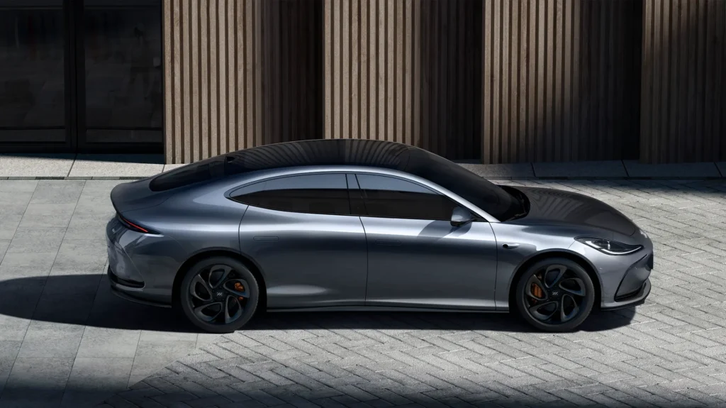 Sølvfarget elbil parkert ved bygg med vertikale trepaneler.