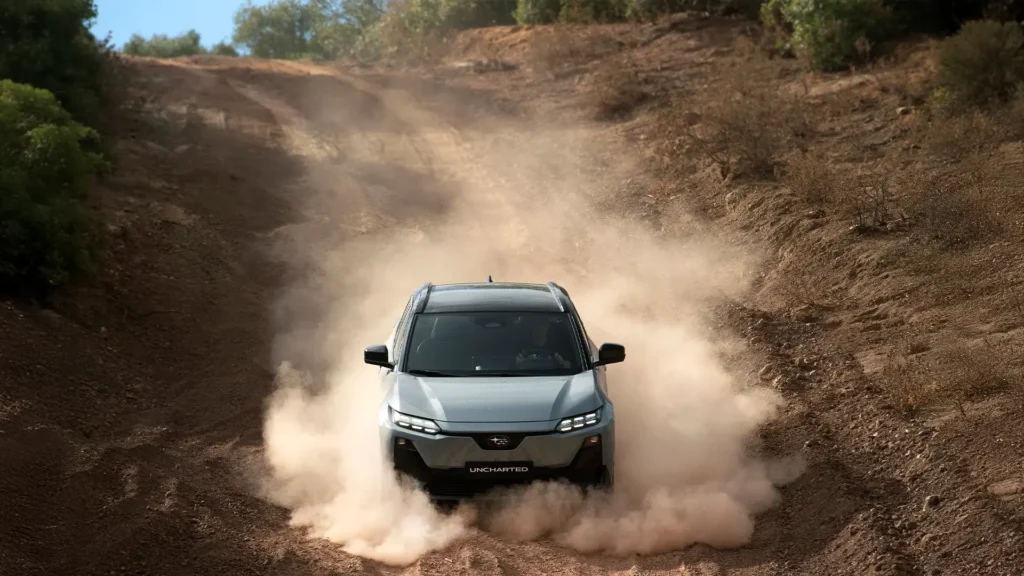 Grå SUV kjører på støvete vei, omgitt av trær og busker.
