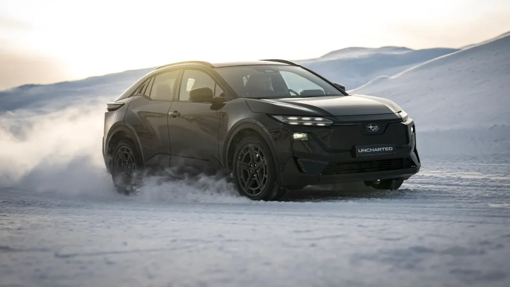 Svart SUV kjører i snø med fjell i bakgrunnen.
