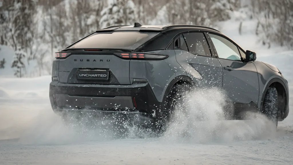 Grå SUV kjører fort gjennom snø foran snødekte trær.