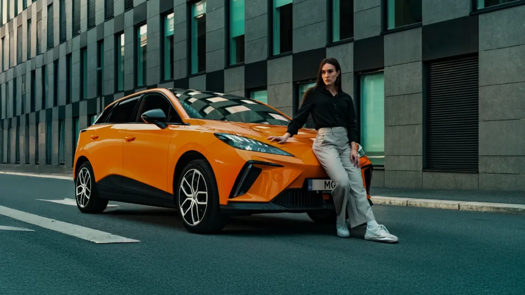 Kvinne lener seg mot oransje bil foran moderne bygning.