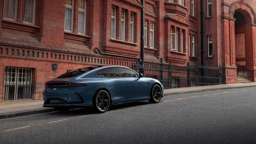 Blå elbil står parkert ved murbygning med ladestasjon.