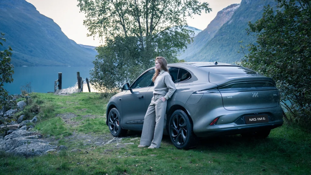 Kvinne ved sølvfarget MG IM6 ved innsjø og fjell.