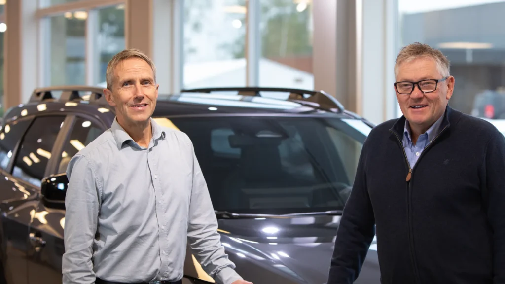 To menn smiler foran en mørk SUV.